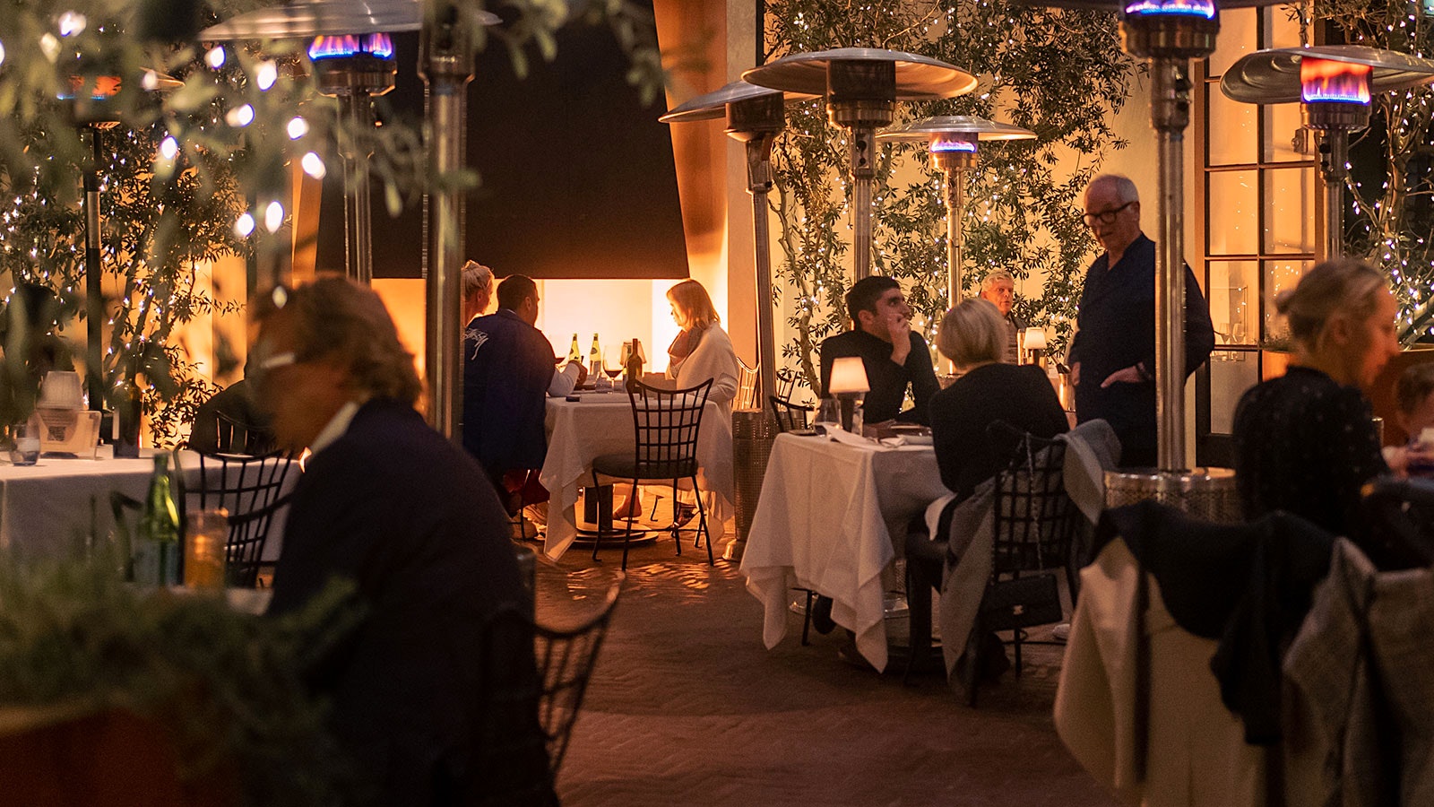 Chef Wolfgang Puck speaking to two guests at Spago Beverly Hills in an outdoor dining area
